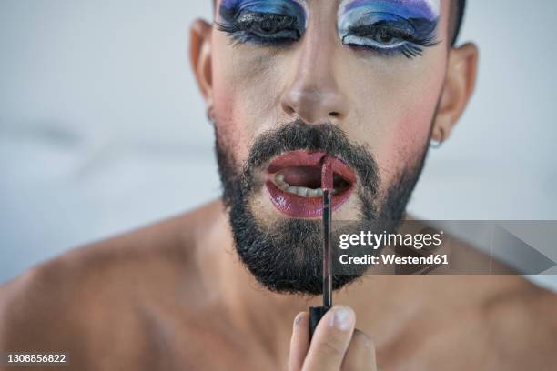 man with blue eye make-up applying lipstick at home - dragqueen stock-fotos und bilder