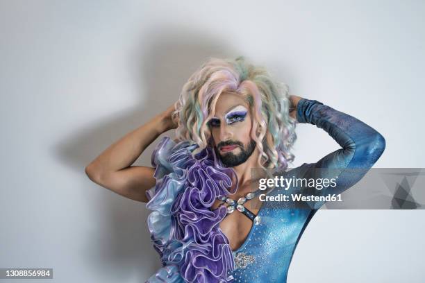 drag queen with hand in hair standing against white wall - drag queens stock pictures, royalty-free photos & images