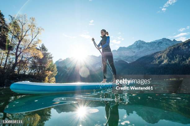 germany, bavaria, garmisch partenkirchen, young woman stand up paddling on lake eibsee - remo em pé imagens e fotografias de stock