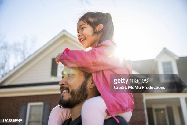 daughter on father's shoulders in front of suburban home - monoparental fotografías e imágenes de stock