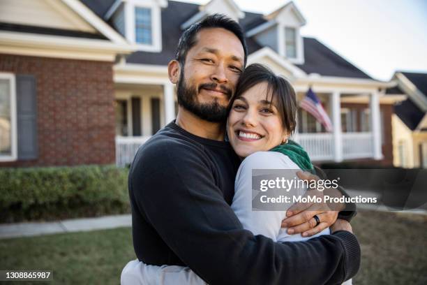 husband and wife embracing in front of home - interracial wife stockfoto's en -beelden