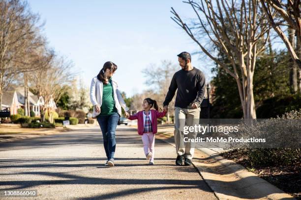 family of three walking in suburban neighborhood - dreiviertel vorderansicht stock-fotos und bilder