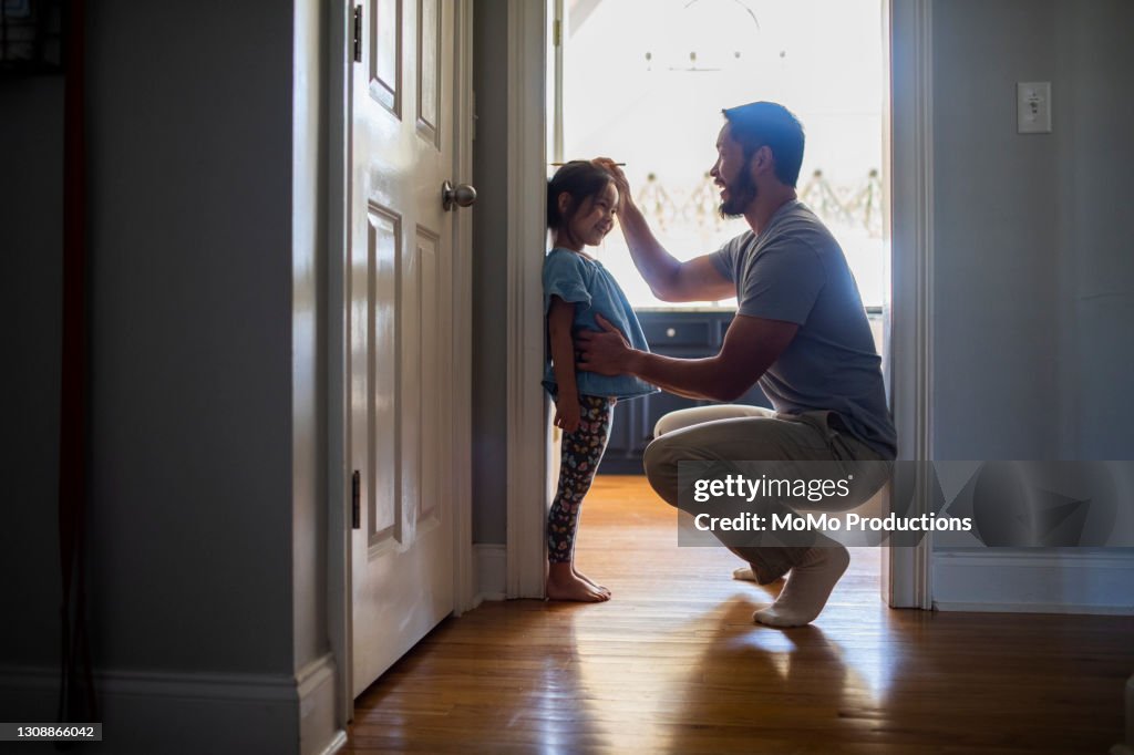 Father measuring daughter's height against wall