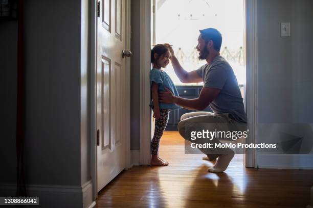 father measuring daughter's height against wall - father foto e immagini stock