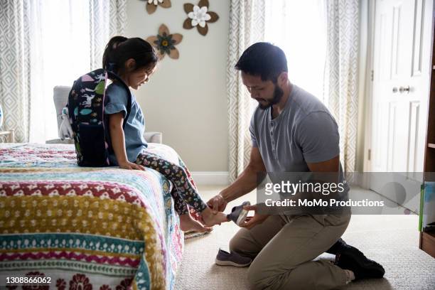 Father helping young daughter put her shoes on