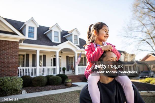 daughter on father's shoulders in front of suburban home - chinese family taking photo at home stock-fotos und bilder
