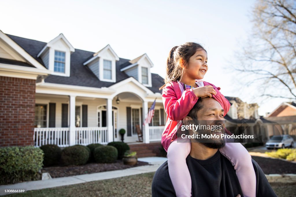 Daughter on father's shoulders in front of suburban home