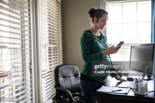 pregnant woman using smartphone in home office - leanincollection ストックフォトと画像