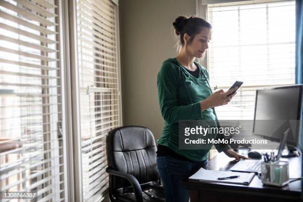 pregnant woman using smartphone in home office - leanincollection stock pictures, royalty-free photos & images