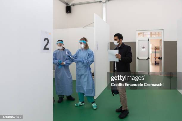 Nurse reads some documents belonging to a young doctor who is going to receive a second dose of the Pfizer Biontech vaccine at a sports center...