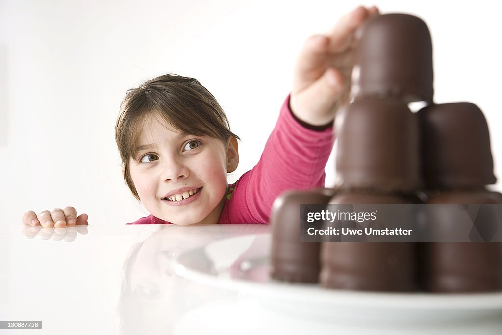 A girl reaching secretly for a chocolate marshmallow