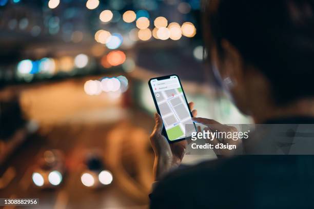 over the shoulder view of young woman using map in mobile app device on smartphone to navigate and search for location in the city at night. travel and navigation concept - woman map stock pictures, royalty-free photos & images