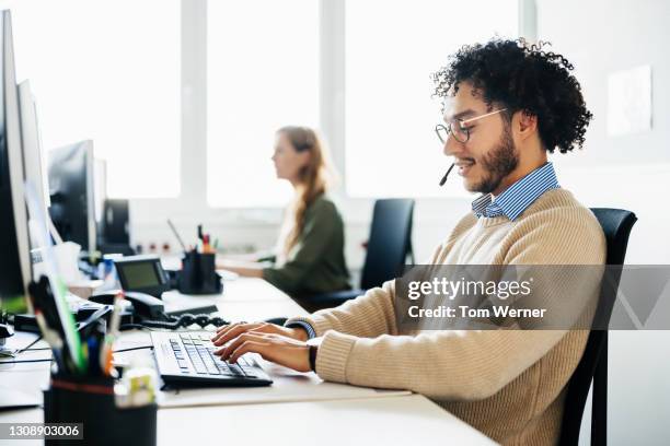 man working at computer and talking to clients on phone - opérateur téléphonique photos et images de collection