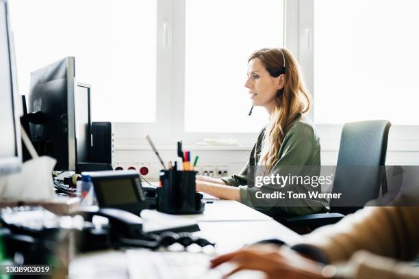 woman busy at work talking to customers on the phone - headset imagens e fotografias de stock