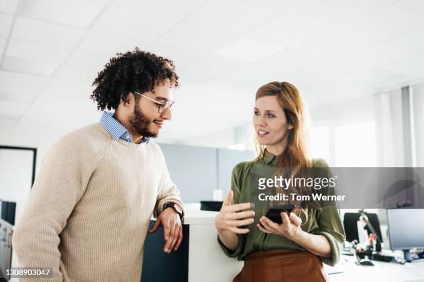 office manager showing colleague something on smartphone - gespräch stock-fotos und bilder