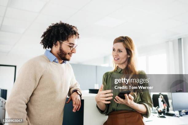 office manager showing colleague something on smartphone - business man and woman stockfoto's en -beelden