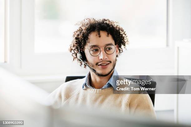 male office employee wearing wireless headset working at computer - employee support stock pictures, royalty-free photos & images