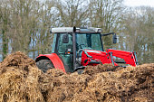 Red tractor with front loader in front of a manure heap