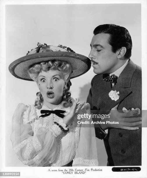 Betty Grable puts her hand up as Cesar Romero holds his heart in a scene from the film 'Coney Island', 1943.
