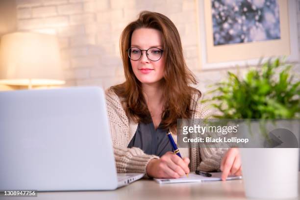 young woman writing notes looking at laptop learning lecture watching a webinar. - online seminar stock pictures, royalty-free photos & images