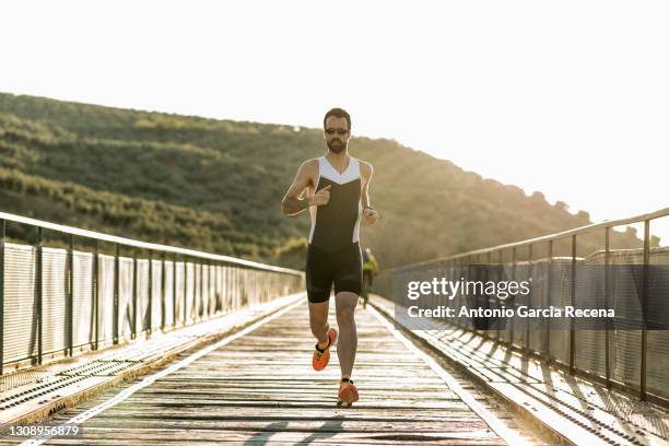 full length portrait of triathlon runner training at sunset on a bridge - triathlet stock-fotos und bilder