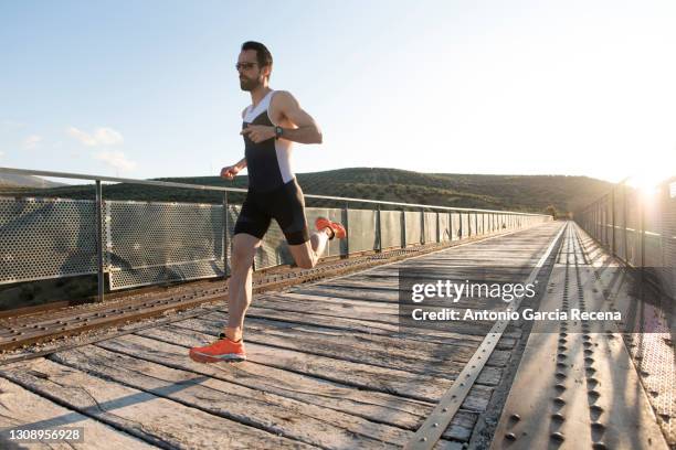 full-length portrait of runner sprinting on a bridge - triathlete stockfoto's en -beelden