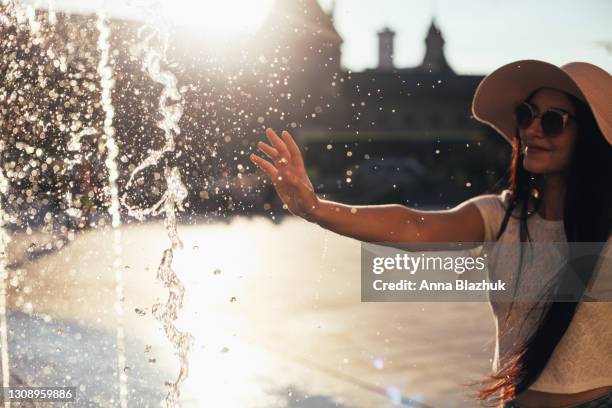 young woman wearing hat playing with fountain water in hot summer sunny day - fountain stock pictures, royalty-free photos & images