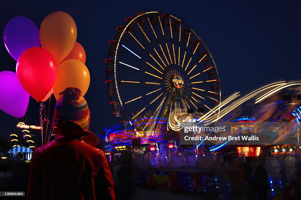 Woman holding balloons overlooking fairground
