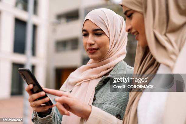 arab female friends using a smartphone outdoors on the street. - arabische frau kopftuch stock-fotos und bilder