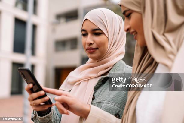 arab female friends using a smartphone outdoors on the street. - etnias de oriente medio fotografías e imágenes de stock