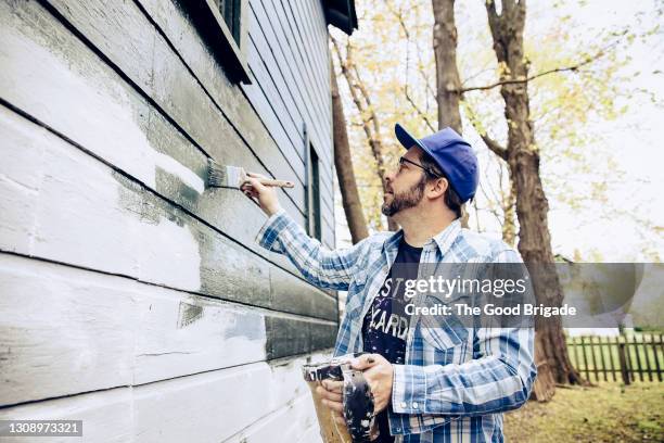 side view of man painting exterior of home - painting house exterior stock pictures, royalty-free photos & images