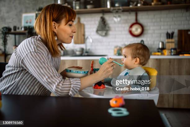 mother feeding baby boy sitting in high chair - baby eating toy stock pictures, royalty-free photos & images