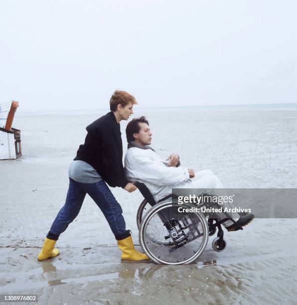 Nach außen hin scheint die Beziehung der Journalistin Thea zu dem gelähmten Nat intakt zu sein. Bild: Thea fährt Nat im Rollstuhl den Strand entlang....