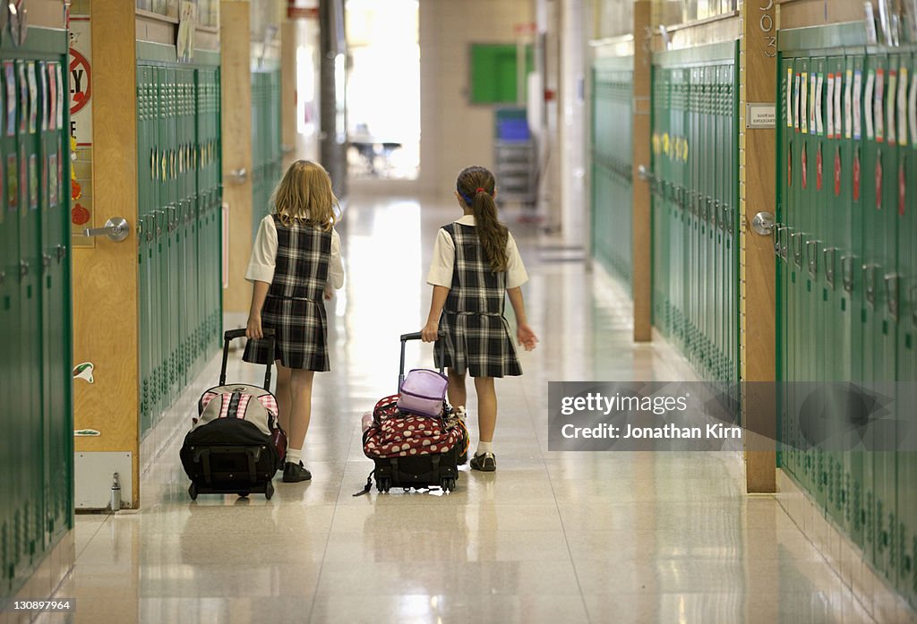 Second grade girls roll backpacks in school.