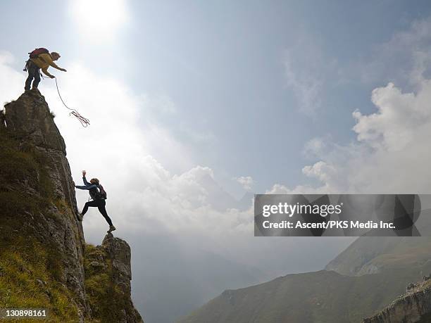 climber throws rope to partner below, above mtns - mountaineering team stock pictures, royalty-free photos & images