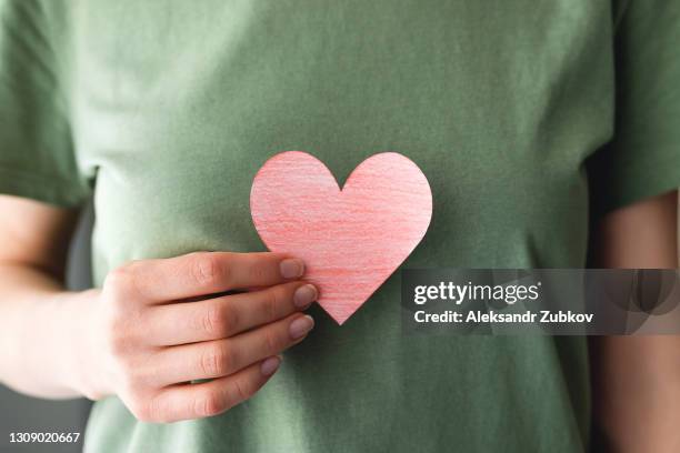 a woman or girl holds a red painted heart or a valentine card cut out of paper. heart on the background of green casual clothing or t-shirt. the concept of valentine's day, a symbol of love and loyalty. - lealdade imagens e fotografias de stock