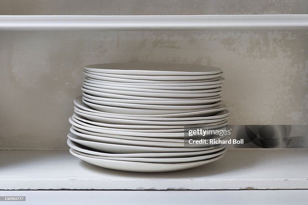 A stack of ceramic dining plates on a shelf.