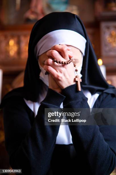 suora che prega in chiesa, indossando una maschera protettiva per il viso. chiudi le mani tenendo perline di rosario. - monastero foto e immagini stock