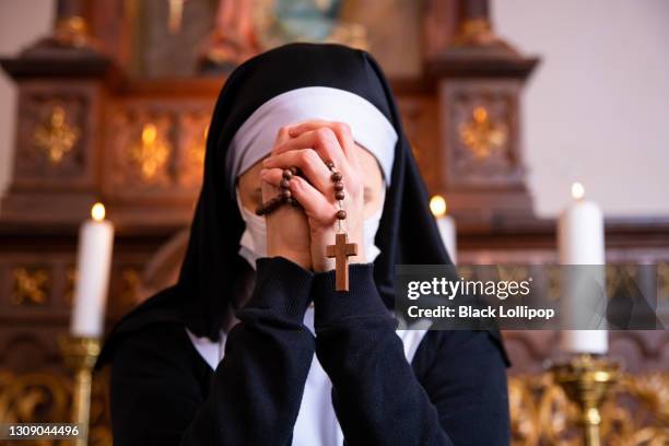 een non die haar hoofd in gebed buigt. sluit omhoog op handen die rozenkransparels houden. - zuster stockfoto's en -beelden