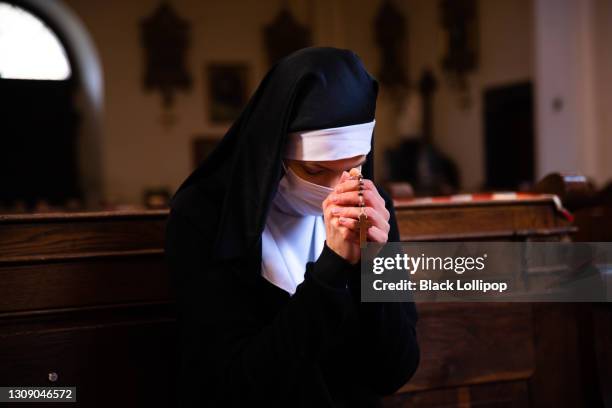 una monja inclinando la cabeza en oración sentada en una iglesia con máscara protectora. - monja fotografías e imágenes de stock