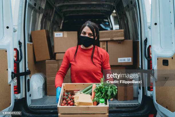 portrait of a delivery woman with a fruit and vegetable crate in front of her delivery van - food bank stock pictures, royalty-free photos & images