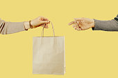 Select focus of one hand of the woomen is passing a craft paper bag to the other hand. Concept of thrift stores, resale, second hand.