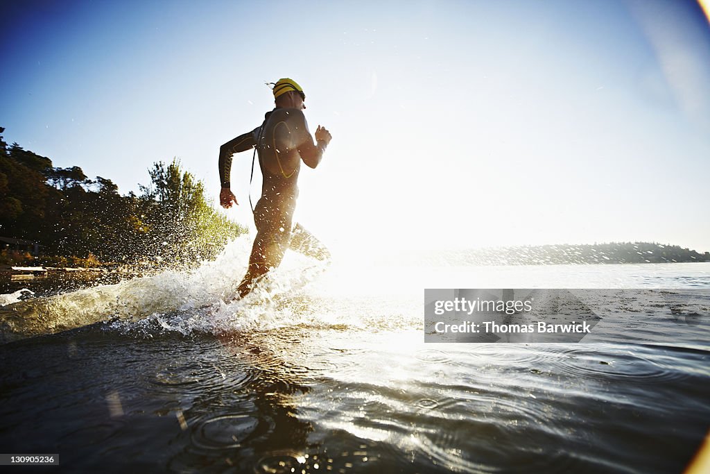 Male triathlete running into water at sunrise