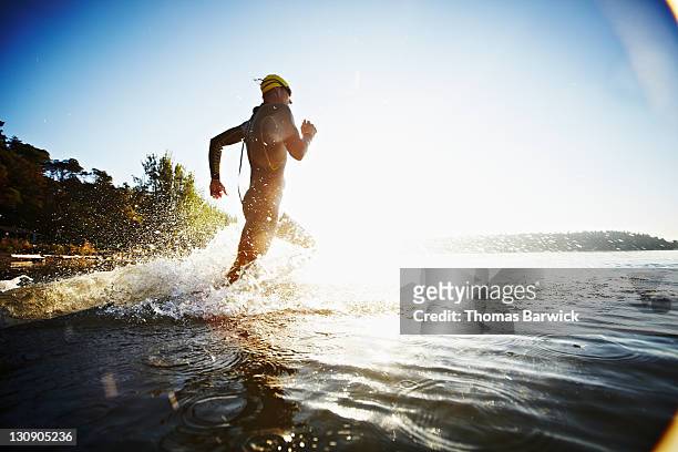 male triathlete running into water at sunrise - トライアスロン ストックフォトと画像