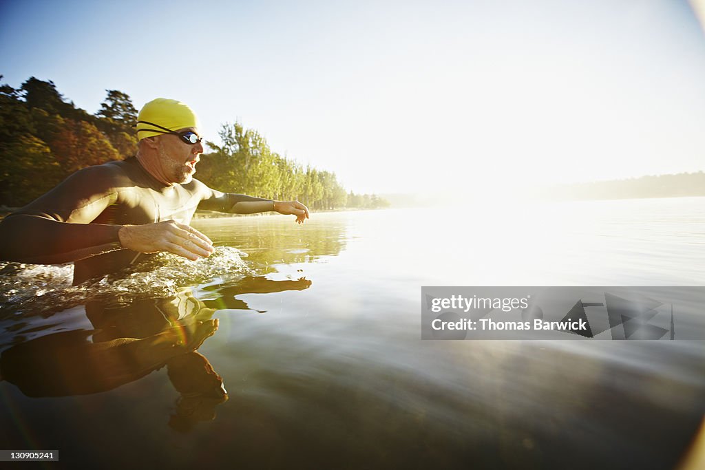 Male triathlete diving into water at sunrise