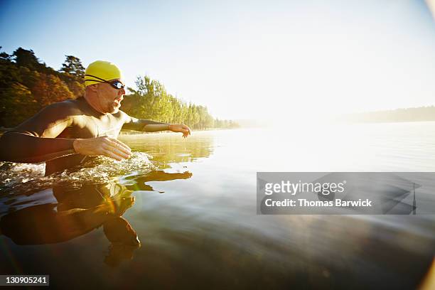 male triathlete diving into water at sunrise - beginner triathlon stock pictures, royalty-free photos & images