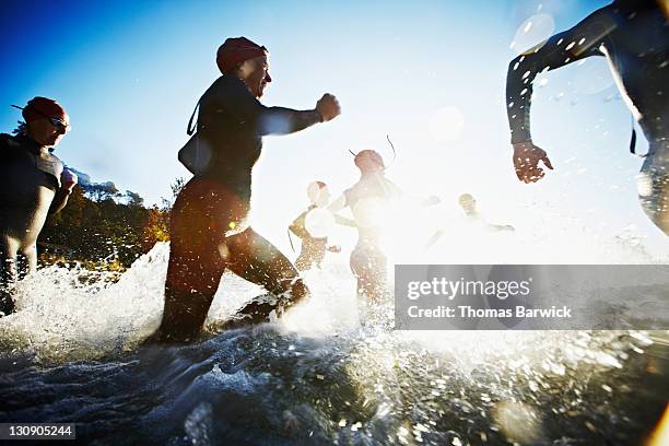 group of triathletes running into water at sunrise - triathlon stock-fotos und bilder