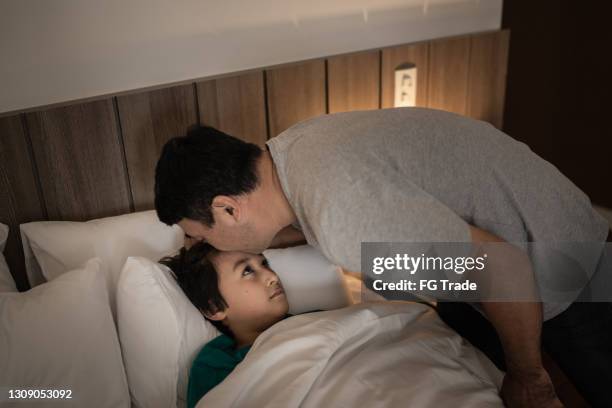 father putting son to sleep and giving him a kiss in the forehead - good night imagens e fotografias de stock