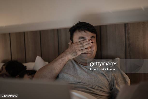 tired man working in bed while kids are sleeping beside him - man rubbing eyes stock pictures, royalty-free photos & images