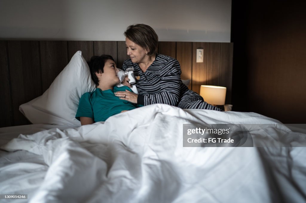 母親在吸入治療期間幫助兒子使用霧化器